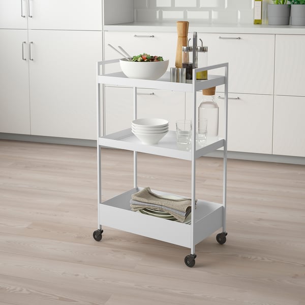 NISSAFORS metal trolley with 3 shelves in kitchen holding salad, plates, glasses, and towels.