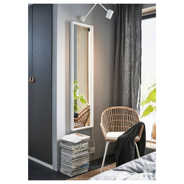 Minimalist bedroom with gray walls, large NISSEDAL mirror in white frame, wicker chair, gray curtains, and stacked magazines on floor.