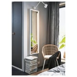 Minimalist bedroom with gray walls, large NISSEDAL mirror in white frame, wicker chair, gray curtains, and stacked magazines on floor.