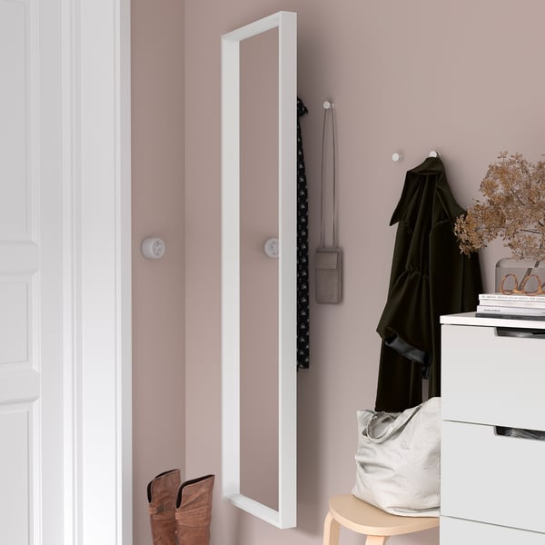 A mirrored cabinet on a pink wall with coat hook. Underneath, a stool holds a bag and boots, next to a drawer with books and dried flowers.