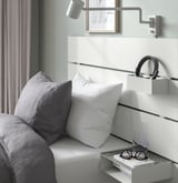 Modern bedroom setup featuring a bed with soft gray and white pillows, a wall-mounted headboard with integrated shelf and reading light.