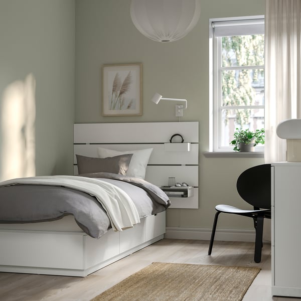 Minimalist bedroom with white NORDLI bed, green wall, large window, high headboard, storage drawers, wall light, black chair, rug, potted plant.