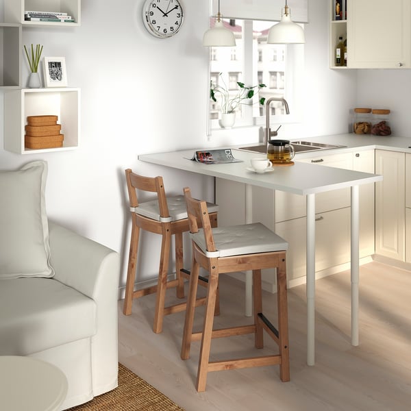 Kitchen with white counters, NORDVIKEN light grey stools, sink, cups, teapot. Minimalist decor with white cabinets and light grey couch.