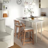 Kitchen with white counters, NORDVIKEN light grey stools, sink, cups, teapot. Minimalist decor with white cabinets and light grey couch.