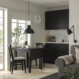 Modern black dining set with foldable leaf table and chairs. Large window, vibrant greenery, and a sleek black kitchen.