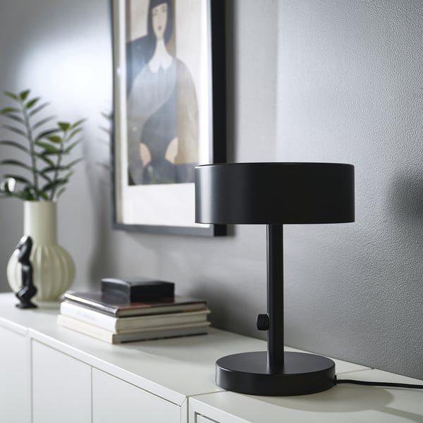 NYMÅNE black lamp on white cabinet with books and plant.