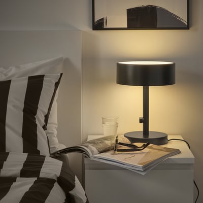 NYMÅNE lamp on bedside table with striped pillows.