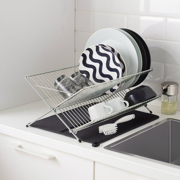 Metal dish rack on a kitchen counter with plates and cups drying; black mat underneath to absorb water.