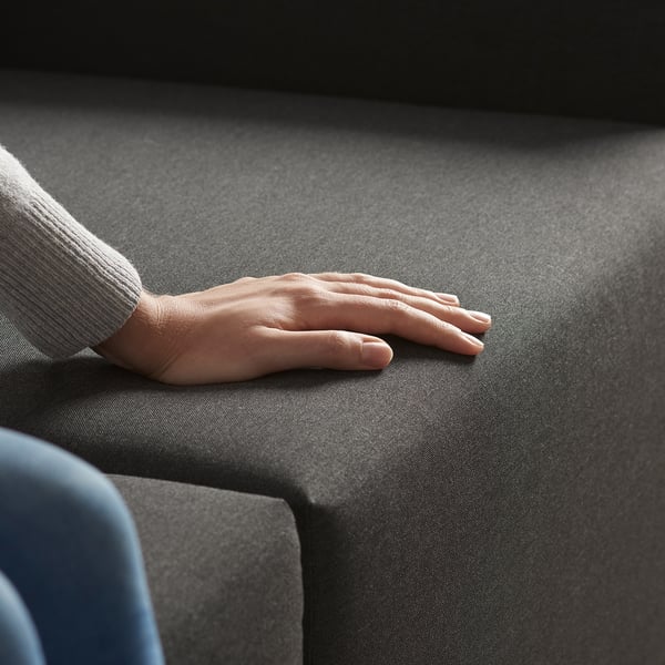 A persons hand rests on a gray sofa sectional. The sofa can convert into a chaise longue.