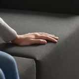 A persons hand rests on a gray sofa sectional. The sofa can convert into a chaise longue.