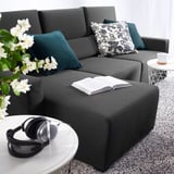 Modern, gray ODENSLUNDA sectional sofa with dark green throw pillows, an open book, and black headphones on a white coffee table near a window.