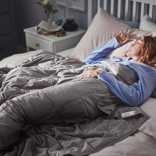 In a person sleeps peacefully under a gray ODONVIDE weighted blanket on a bed with light blue linens, creating a serene atmosphere.