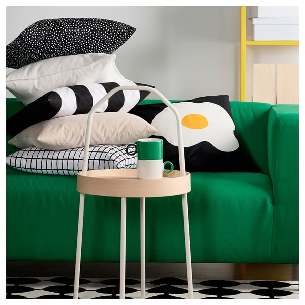Bright green sofa with black & white patterned pillows. Small round white table holds a green mug. Black & white rug beneath.