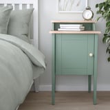 Green ikea olderalen bedside table with books, clock, and plant. Mixes open and closed storage, fitting next to bed.