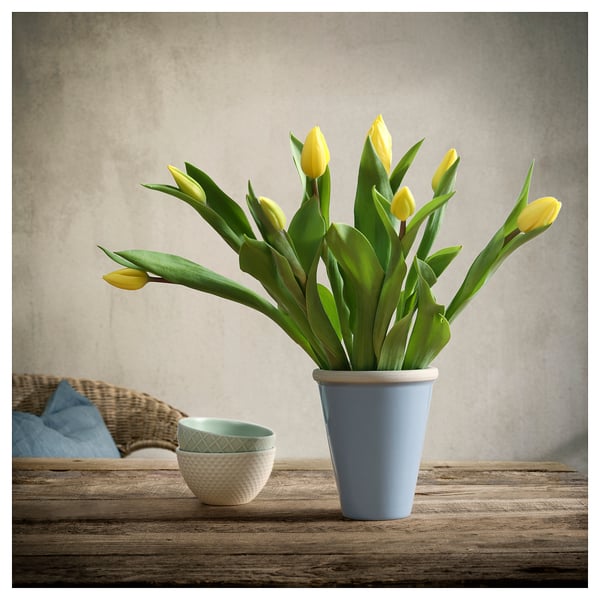 Blue ceramic vase with yellow tulips on wooden table. Rustic, simple design.