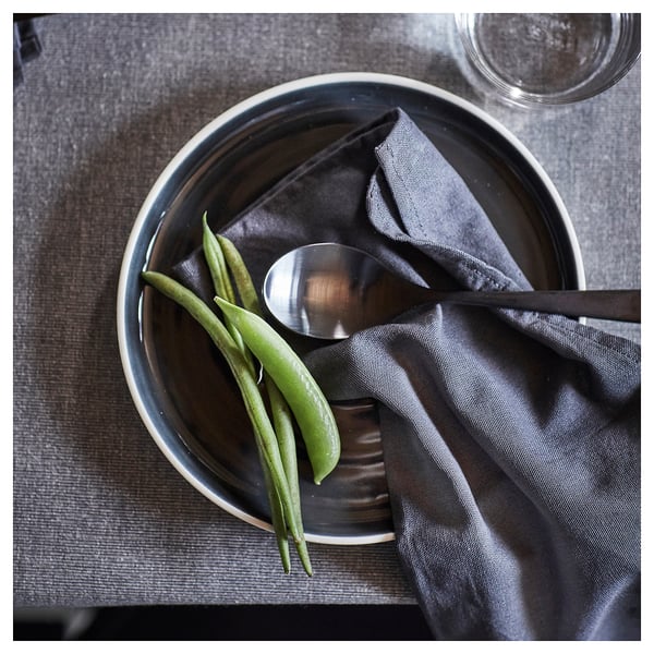 Black bowl with green beans and spoon on dark cloth.