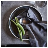 Black bowl with green beans and spoon on dark cloth.