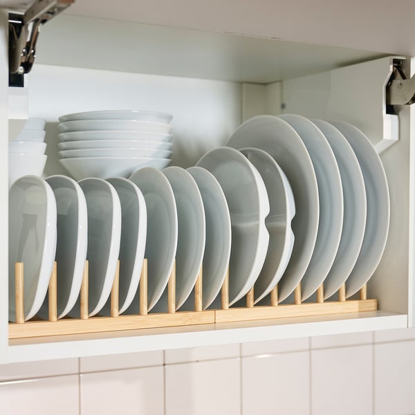 White kitchen shelf with OSTBIT bamboo plate rack, holding multiple white plates, neatly organised and ready for use.
