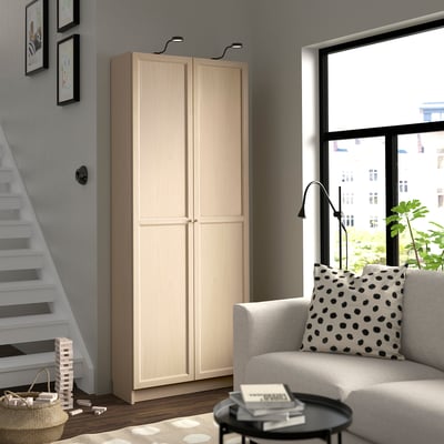 Modern living room: tall OXBERG cream cabinet, black coffee table, white armchair with polka dot pillow. Large window, staircase.