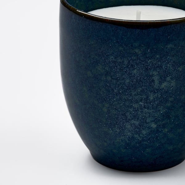 Close-up of a handcrafted, speckled blue-green stoneware candle with visible cotton wick.