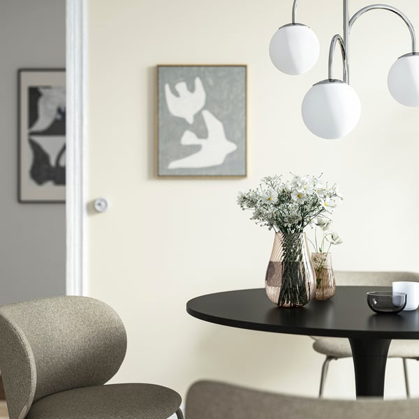 Dining setup with daisies in tall vase, pendant lights, abstract art, grey chairs.