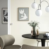 Dining setup with daisies in tall vase, pendant lights, abstract art, grey chairs.