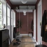 Modern hallway with maroon walls, glass PAX wardrobe, black coat stand, potted plant, boots, and vases.