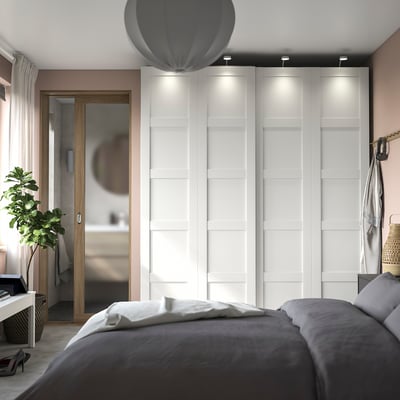 Modern bedroom with PAX wardrobe, sliding doors, grey bedding, wall mirror, hanging lamp, and plant.