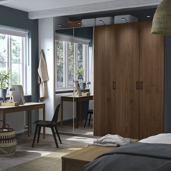 Modern bedroom with large PAX wardrobe in wooden color, beside a desk and black chair, featuring a mirror and woven textiles.