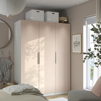 Large beige wardrobe with silver handles in bedroom. Mirror, clothes, window with plant, cozy bed.