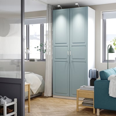 PAX wardrobe in light blue with soft-closing doors near window in cozy room.