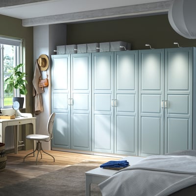 Blue PAX wardrobe dominates room with tall doors, shelves, desk, and bed, reflecting natural light.