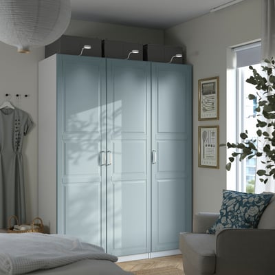 Modern bedroom: blue wardrobe, gray couch, white bed, art. PAX wardrobe fits corner, with storage boxes above and garment hooks.