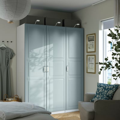 Modern bedroom with blue PAX wardrobe, bed, sofa, large window, mirror, and plant.