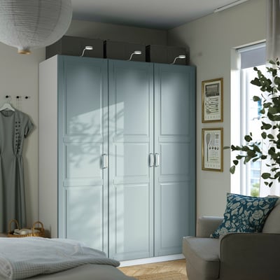 Modern bedroom with large light gray PAX wardrobe, gray chair, brick wall, and plant.