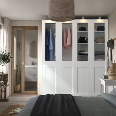 Bedroom with white PAX wardrobe, glass doors, gray bed, wooden mirror, wicker lamp, wall decor.