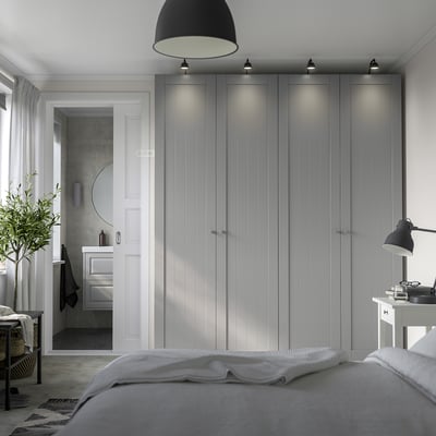 Modern grey PAX wardrobe with soft lighting, larger than bed, beside a white door. .