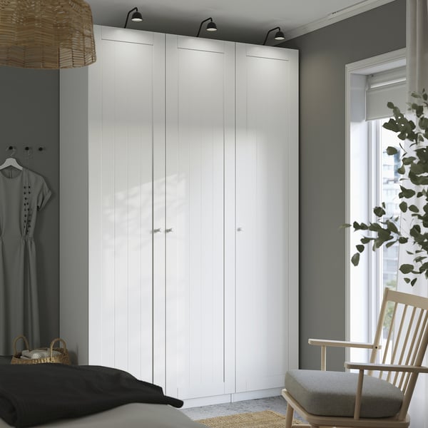 Bright room with large white PAX wardrobe. Bed, chair, and window with plant nearby.