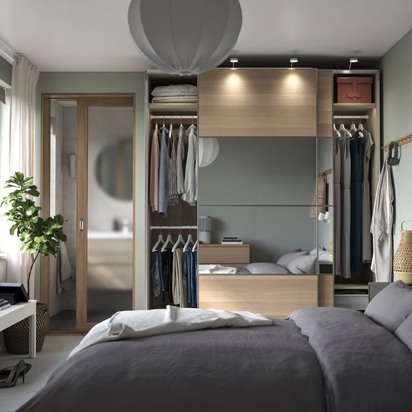 Bedroom with gray bedding, wooden closet, clothes hangers, and a plant.