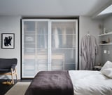 Modern bedroom with gray bedding, a glass-paneled wardrobe, and a gray armchair.