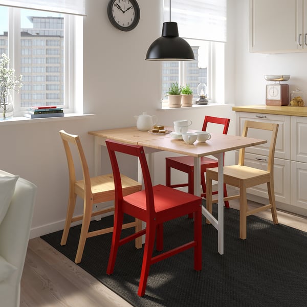 Bright kitchen with white cabinets, a wooden table, red chairs, and a black clock.
