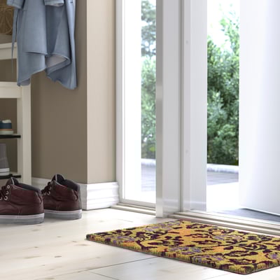 Brown and blue PLATSMÄRKE door mat near white door.