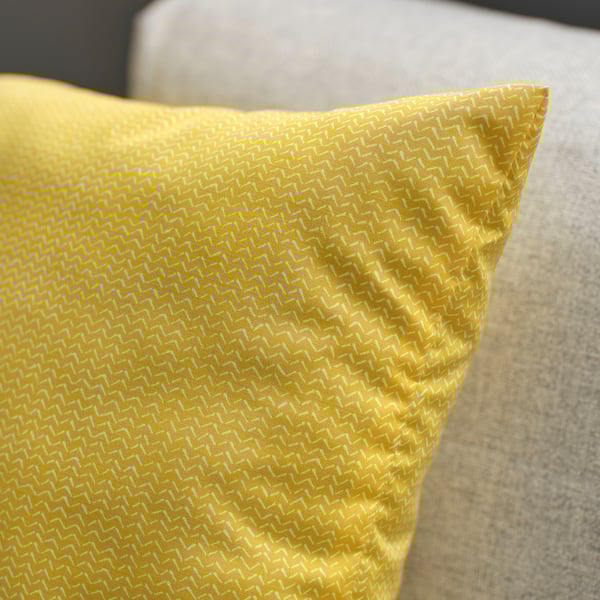 Bright yellow cushion with intricate weaved pattern, placed on a soft beige surface.