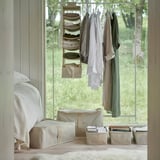 Bedroom with bed, window, and clothing rack. Beige organizers hold folded clothes; under-window storage for seasons.