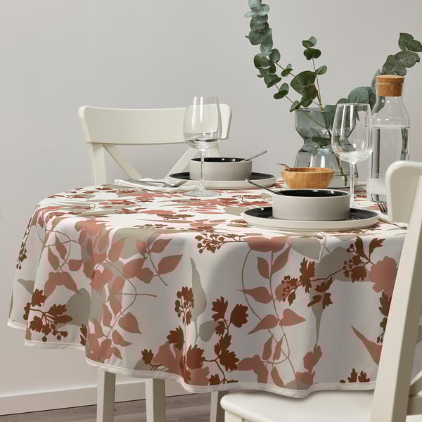Recycled polyester tablecloth with leafy pattern on earthy-toned table, surrounded by white chairs, decorated with greenery, wine glasses, and plates.