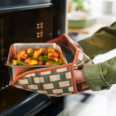 Person pulling roasted veggies from oven with checkered oven mitt.