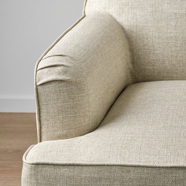 Modern, light-colored armchair with elegant, textured fabric and subtle piping detail, sitting on wooden floor.