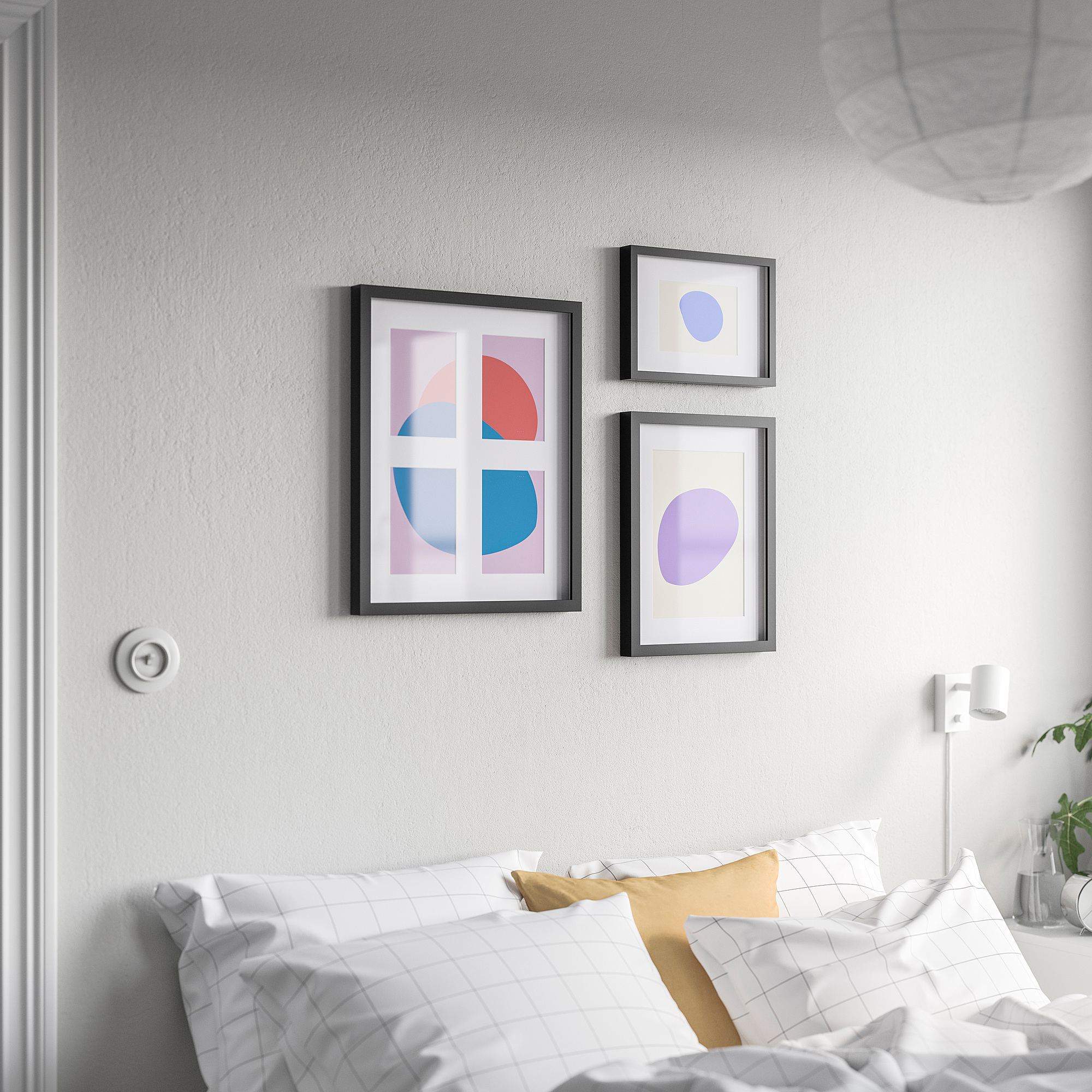 Three framed artworks above bed with checkered pillows: one large multicolored, two lavender abstracts, black modern frames, grey wall.