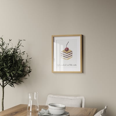Framed cake poster on wall above wooden table with plant and cups.