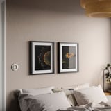 Bedroom with white bed, two black-framed sunflower pictures on wall above, hanging lamp, nightstand with bulb and plant.